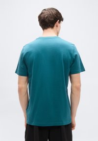 Τιρκουάζ κοντομάνικο μπλουζάκι με στρογγυλή λαιμόκοψη, κατασκευασμένο από μαλακό βαμβάκι, με άνετη εφαρμογή και ομαλή, ομοιόμορφη υφή.