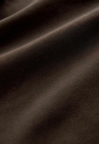 Hnedá tkanina s hladkou textúrou a jemným ribbovaným vzorom, s náznakom lesku a rôznymi odtieňmi. Materiál sa javí ako flexibilný.
