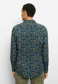 Langes, ärmelloses Hemd mit Blumenmuster in Marineblau mit grünen, gelben und pinkfarbenen Mustern. Verfügt über einen spitzen Kragen und eine lockere Passform.