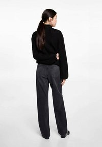 Čierny pletený sveter s vysokým golierom a širokými rukávmi, kombinovaný s tmavozelenými voľnými nohavicami s vysokým pásom.