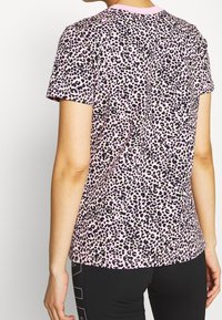 Kortärmad rosa t-shirt med ett svart och grönt leopardmönster, tillverkad av mjuk bomull med rund halsringning och avslappnad passform.