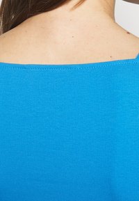 Blå ribbad topp med bred halsringning, slät textur och en åtsittande design som framhäver axlarna och ryggen.