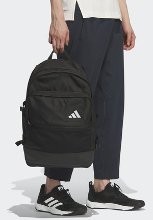 Černý batoh z odolného materiálu s texturovaným povrchem, s výrazným bílým logem Adidas a několika kapsami na zip.