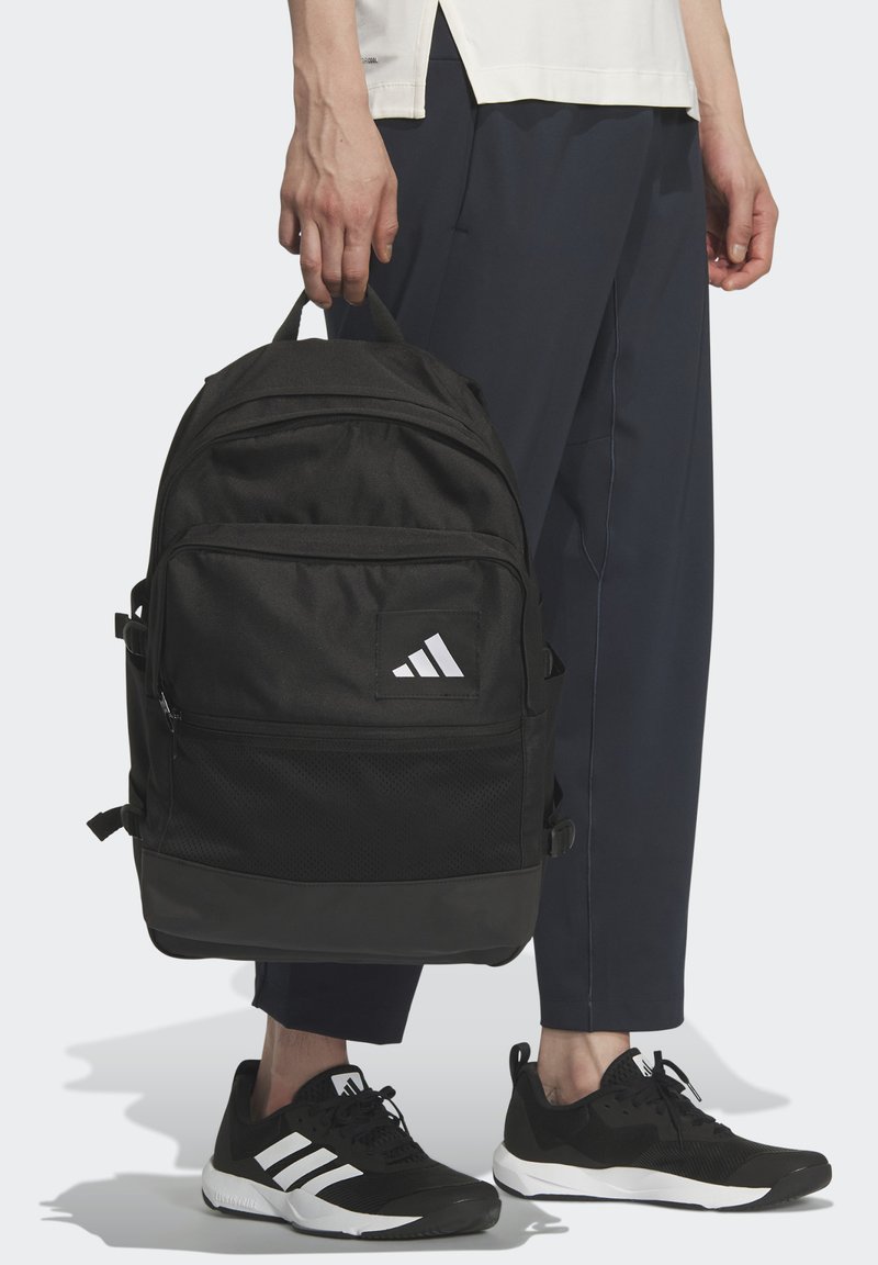 Mochila negra hecha de material duradero con un acabado texturizado, que presenta un prominente logotipo blanco de Adidas y varios compartimentos con cremallera.