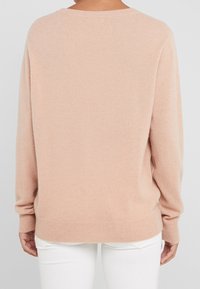 Pull doux rose blush en maille avec encolure ronde, poignets et ourlet côtelés, offrant une coupe décontractée et une texture lisse.