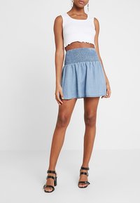 Jupe à rayures bleues avec taille froncée ; design fluide. Associée à un haut court blanc et des sandales à talons hauts noires.