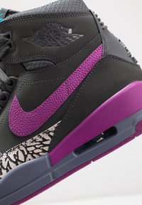 Baskets Air Jordan noires et violettes avec un swoosh Nike violet texturé et des motifs gris et noirs sur le bord de la semelle.