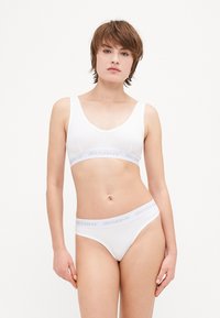 Ensemble de bralette et de thong blanc en tissu lisse. La bralette présente un décolleté arrondi et une bande large avec la marque "MISBHV".