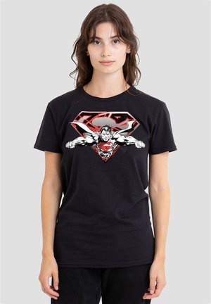 Woman wearing a black T-shirt with a graphic of Superman flying forward inside a stylized red and white Superman logo.