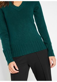 Maglione teal a scollo a V con maniche lunghe, polsini e orlo a costine. Realizzato in morbido materiale a maglia, presenta un colletto texturizzato e un design aderente.