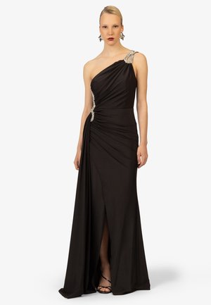 Abito nero a spalla unica realizzato in tessuto drappeggiato, con uno spacco alto fino alla coscia, decorato con accenti di cristallo sulla spalla e in vita.