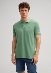 Polo shirt in cotone verde con colletto, patta con due bottoni e maniche corte. Presenta un piccolo logo sul petto e una vestibilità comoda.