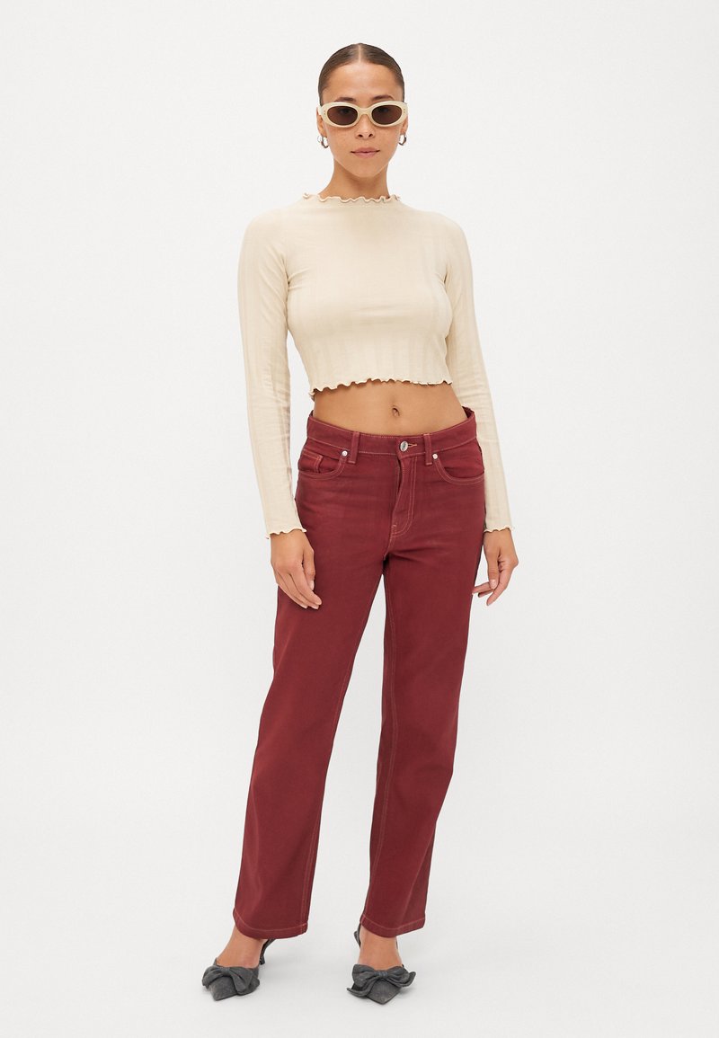 Beige ribbet langærmet crop top med bølget kant, parret med højtaljede, burgunder lige ben jeans. Lyserøde solbriller, flade grå sko.