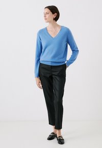 Maglione azzurro chiaro a V, realizzato in materiale morbido, abbinato a pantaloni neri su misura. Mocassini neri con dettaglio in catena dorata.
