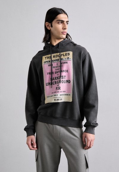 Hoodie gris foncé en coton avec un graphique imprimé en rose et beige. Doté d'une capuche avec cordon de serrage et d'une coupe décontractée. Associé à un pantalon gris clair.