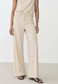 Beige wide-leg pants made of soft fabric, featuring a drawstring waist and smooth texture, paired with black open-toe sandals.