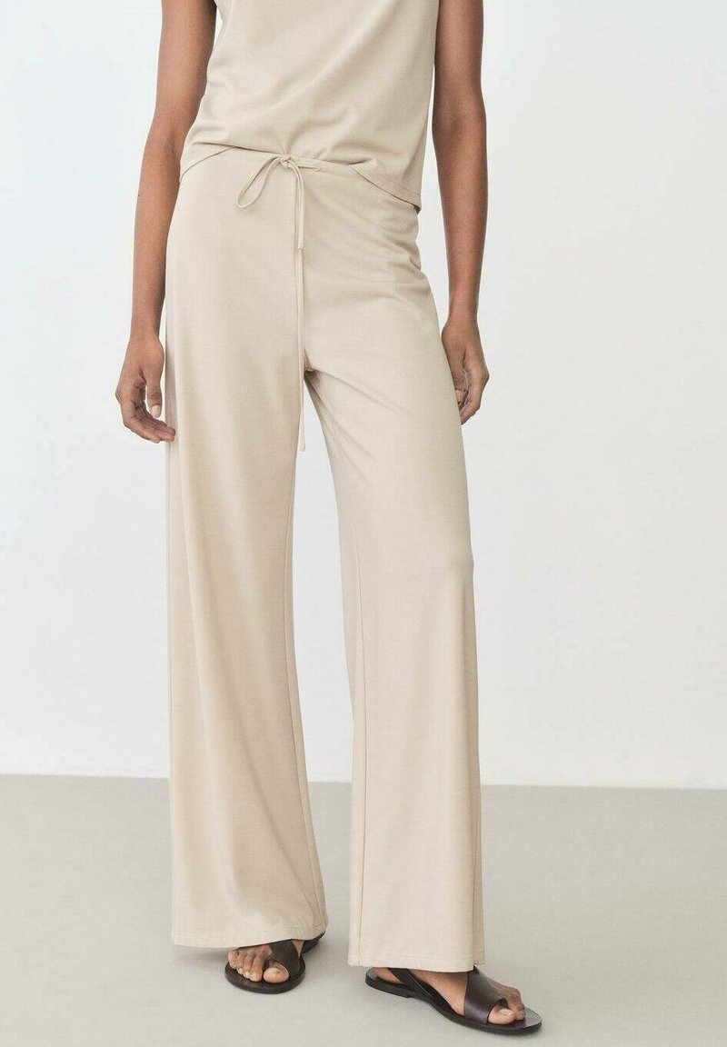 Beige wide-leg pants made of soft fabric, featuring a drawstring waist and smooth texture, paired with black open-toe sandals.