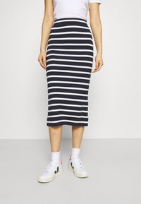 Kvinna iklädd en marinblå och vit horisontellt randig midikjol, vita strumpor, vita sneakers och en vit t-tröja med kort ärm.