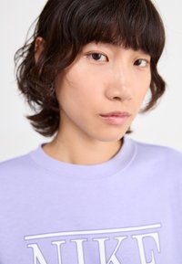 Sweatshirt violet clair avec le logo blanc "NIKE". Tissu doux, design à col rond, texture subtile, capturé en gros plan.