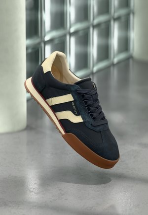 Navy plave tenisice s kremastim prugama, od brušene kože i kože, s gumenim potplatom i teksturiranim završetkom. Imaju dizajn s vezicama.