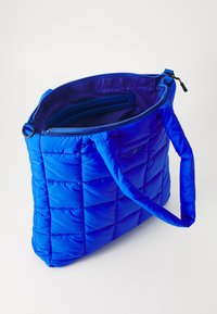 Sac fourre-tout bleu matelassé avec une texture rembourrée, fermeture éclair et poche intérieure, doté de deux poignées et d'une finition brillante.