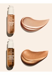 To dråpeflasker med Sol de Janeiro Glowmotions Glow Oil med matchende bronse- og gyldne oljesmaker på en beige bakgrunn.