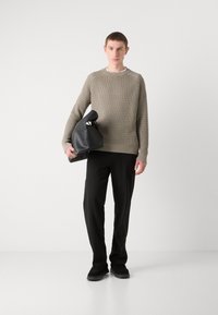 Grau strukturierter Pullover, schwarze Hose und schwarze Tasche. Der Pullover hat ein geripptes Muster, und die Tasche hat eine einzigartige Form mit einer glatten Oberfläche.