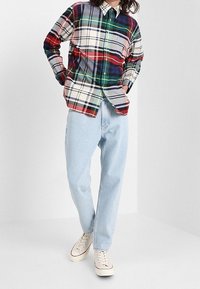 Camicia a quadri multicolore (rosso, blu, verde) con colletto button-down, abbinata a jeans azzurri chiari e sneakers color crema.