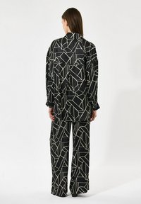 Črna vzorčasta srajca in široke hlače, ki vsebujejo geometrijski kremni vzorec, gladko teksturo in sproščen kroj z dolgimi rokavi.