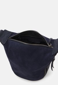 Sac à épaule en suede marine avec une fermeture éclair supérieure, des accents texturés et un intérieur doublé. Il présente une forme effilée et une poche zippée sur le côté.