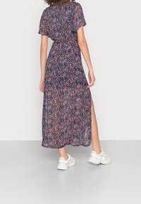 Abito maxi con sfondo navy, stampa floreale in rosa e bianco, maniche corte e orlo spaccato. Indossato con sneaker bianche.