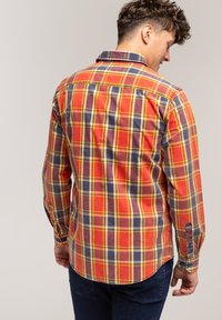 Czerwona, pomarańczowa i żółta koszula w kratę z długim rękawem, z kołnierzykiem zapinanym na guziki i zaokrąglonym dołem; tkanina bawełniana o zróżnicowanej fakturze i detalach przeszyć.