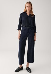 Blusa blu navy con colletto, abbinata a jeans a gamba larga blu scuro. L'outfit è completato da mocassini neri, con dettagli minimi.