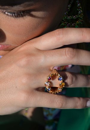 Gold ring featuring a teardrop shape, adorned with colorful rhinestones in red, blue, and yellow, set in a scalloped design.
