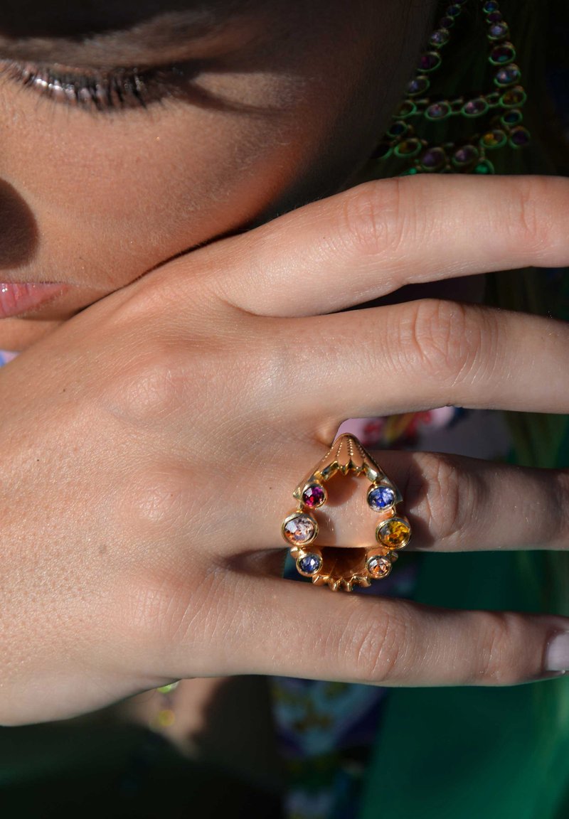 Gold ring featuring a teardrop shape, adorned with colorful rhinestones in red, blue, and yellow, set in a scalloped design.