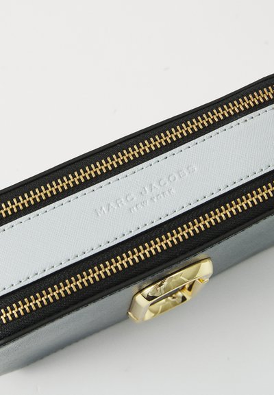 Juodas ir sidabrinis rankinukas su auksiniu užtrauktuku, turintis baltą skydelį su įspaustu užrašu "MARC JACOBS NEW YORK" ir aukso spalvos apdailos akcentu.