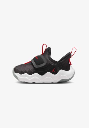 Sneaker nera con tomaia testurizzata, accenti rossi, cinturino regolabile, suola ondulata bianca e logo nero sul lato.