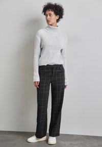 Grauer gerippter Rollkragenpullover mit strukturiertem Design, kombiniert mit schwarzen karierter weit geschnittenen Hosen. Weiße Turnschuhe runden das Outfit ab.