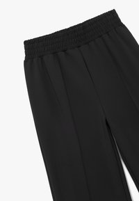 Pantalones negros de cintura elástica con una textura suave, que cuentan con pliegues en la parte frontal para un detalle de diseño adicional.
