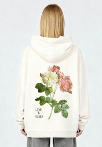 Sudadera con capucha color crema con un gráfico floral de rosas rosas y blancas con hojas verdes, texto "LOVE & ROSAS" en fuente oscura en la parte inferior.