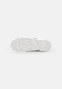 Semelle de sneaker blanche en caoutchouc texturé, avec des éléments surélevés et un design incurvé. Surface lisse avec un détail de logo près du talon.