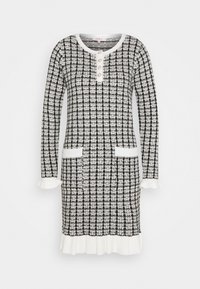 Abito lavorato a maglia in un motivo pied de poule bianco e nero, con maniche lunghe, una patta di bottoni, due tasche frontali e un orlo a balze.