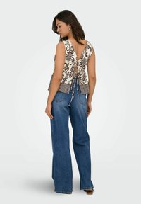 Vue arrière d'un haut sans manches à motif crème et marron, avec un décolleté en V profond et une fermeture à nouer, associé à un jean bleu évasé.