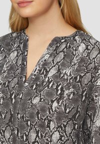 Zwart-wit slangenprint blouse met een V-hals, zachte stof en een gestructureerd patroon. Close-up afbeelding met focus op de details van de halslijn.