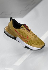 Gul mesh sneakers med sorte detaljer, der har et rødt Nike-swoosh, struktureret overdel og polstret sål, der fremviser et moderne design.