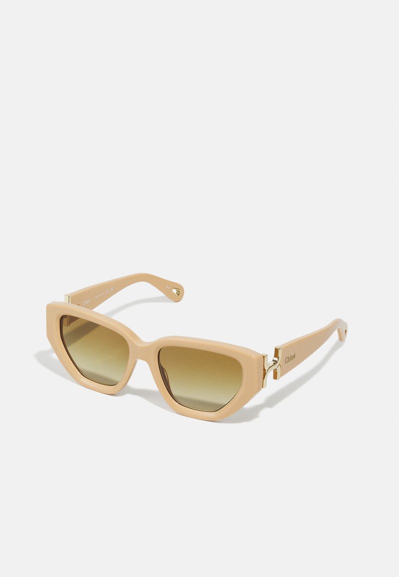 Beige sunglasses with a geometric shape, gradient brown lenses, and gold-tone hardware accents on the temples. Stylish and modern design.