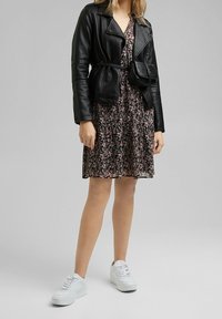 Chaqueta de cuero negra con detalles acanalados en las mangas, vestido floral en negro, rosa y blanco, combinado con zapatillas blancas y un bolso pequeño negro.