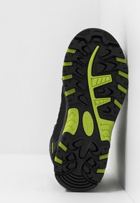 Svart sneaker sula med gröna accenter, med ett texturerat mönster för grepp och en ovandel i mesh med ventilationshål.