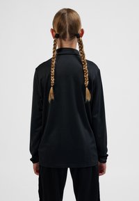 Svart långärmad skjorta med krage, med en slät textur och avslappnad passform. Flätat hår syns bakifrån.