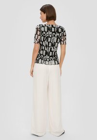 Zwart short-sleeve sheer top met grijs abstract patroon, gegolfde zoom, gepaard met wijde witte broek. Gestructureerd materiaal, lichtgewicht ontwerp.